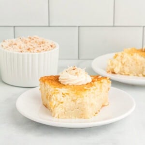 Slice of crustless coconut pie on a white plate topped with whipped cream and toasted coconut.