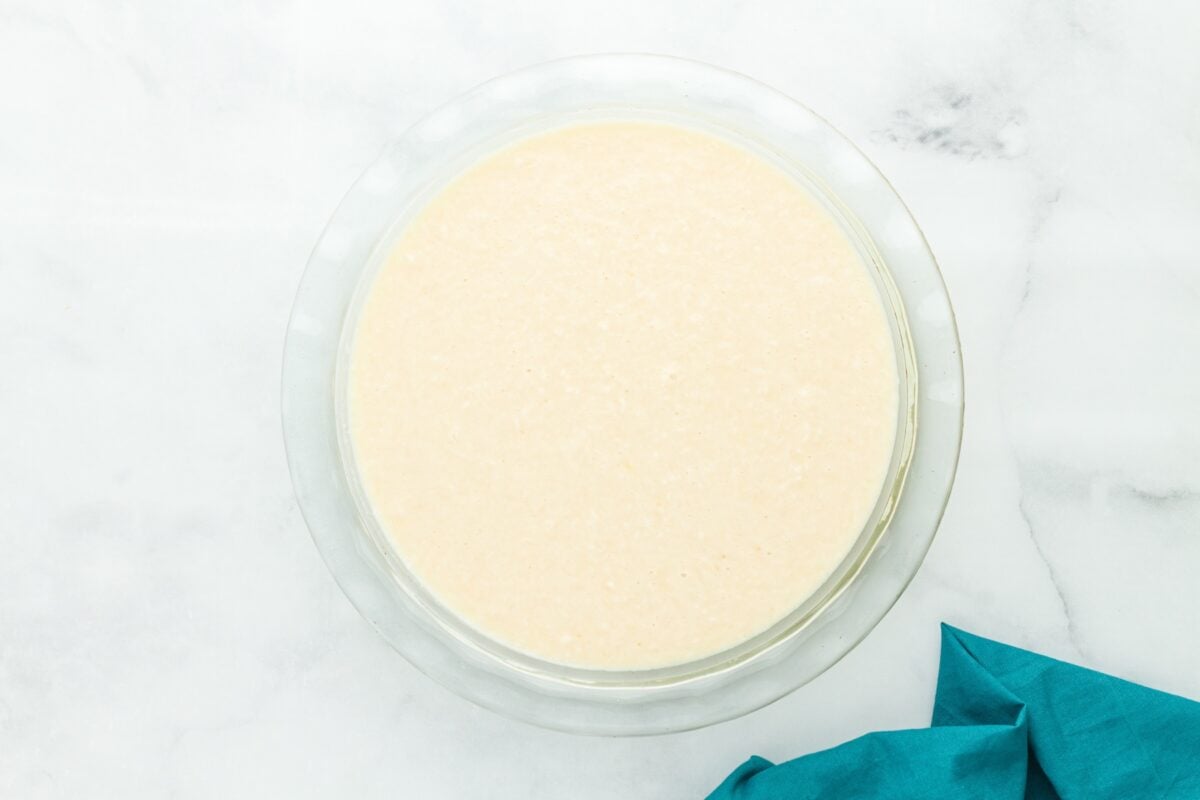 Crustless coconut pie batter poured into a 9-inch glass pie dish before baking.