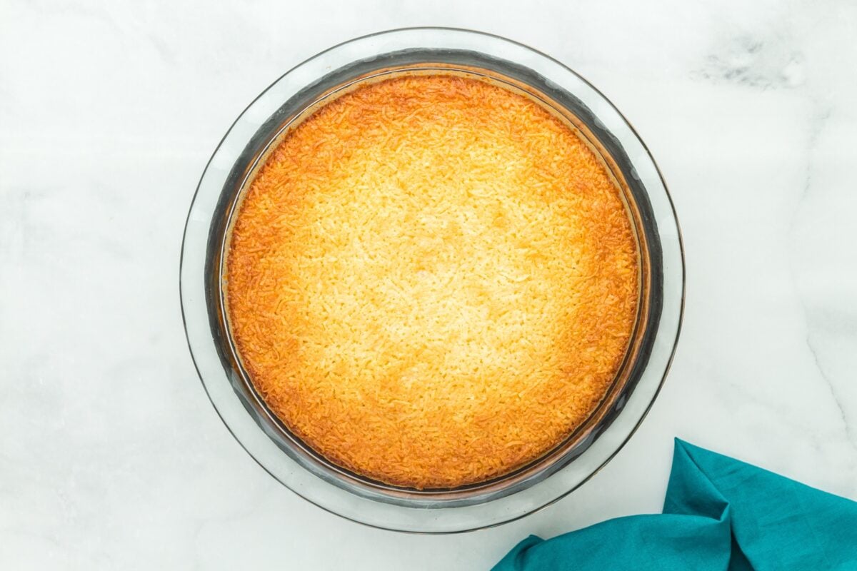 Golden-brown crustless coconut pie fresh out of the oven cooling in the pie dish.