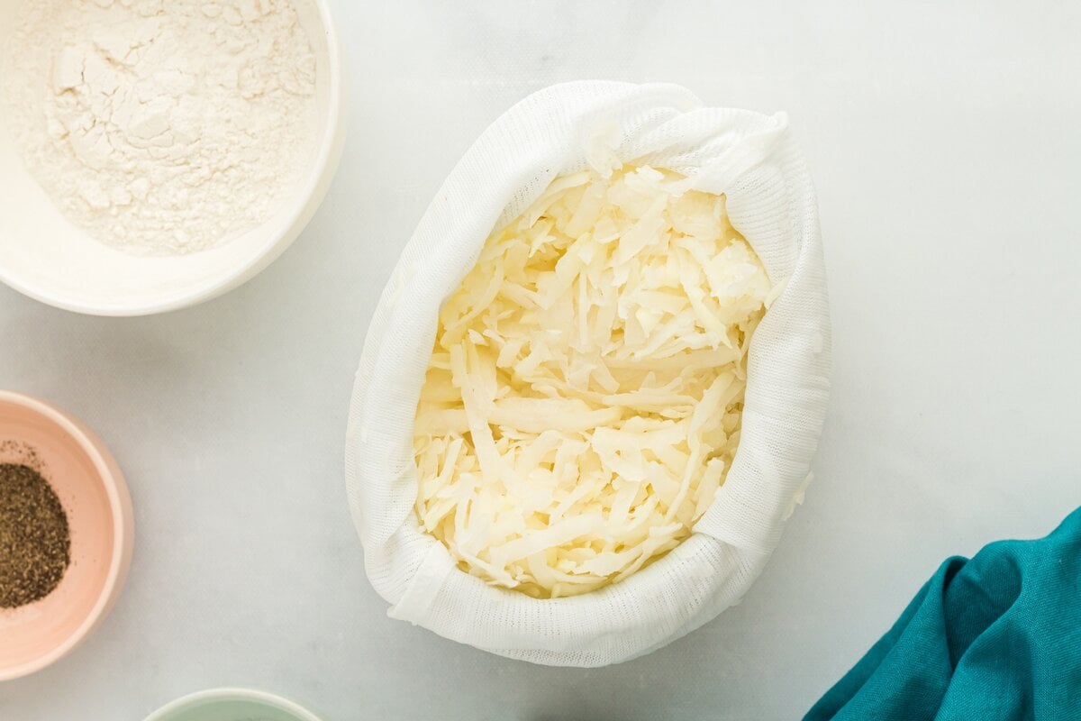 Grated potatoes wrapped in cheesecloth, ready to be squeezed to remove moisture.
