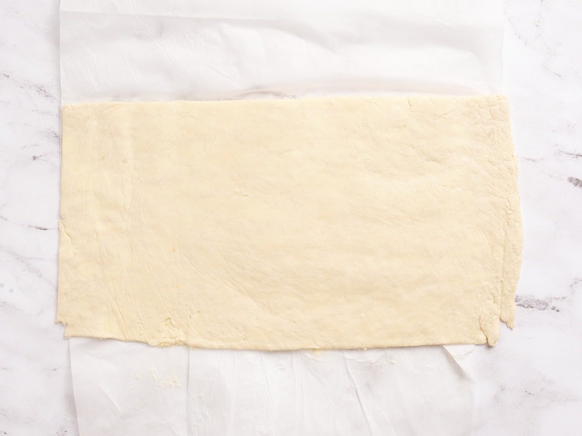 Rolled out gluten free laminated dough resting between sheets of parchment paper before cutting.