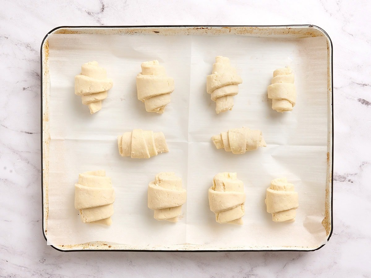 Unbaked gluten free croissants rolled and arranged on a parchment-lined baking sheet.