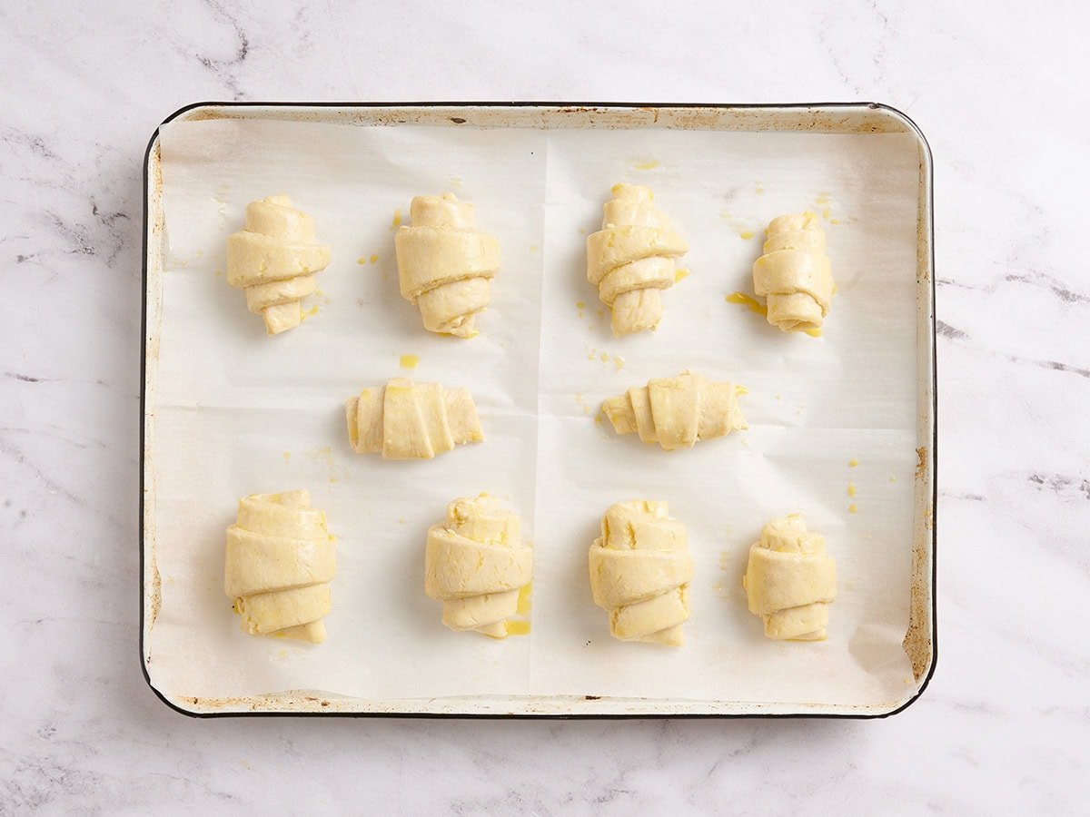 Shaped gluten free croissants brushed with egg wash on a parchment-lined baking pan.