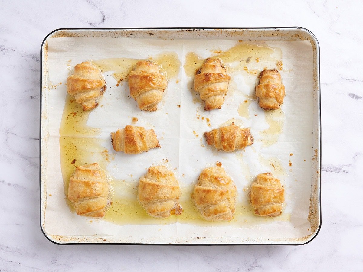 Freshly baked gluten free croissants on a sheet pan with melted butter pooled around the edges.