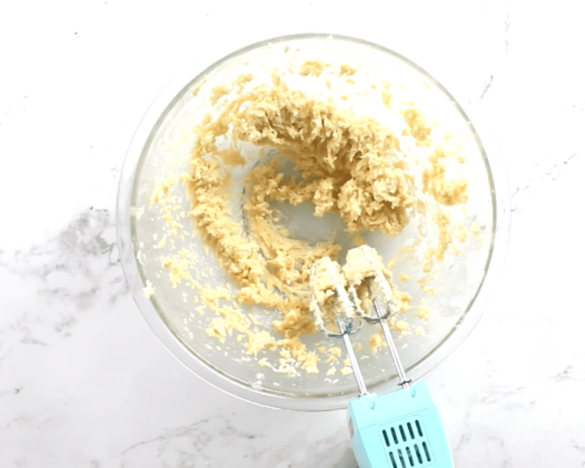 Butter, sugars, egg yolk, and vanilla mixed together into a smooth cookie dough base in a glass bowl.