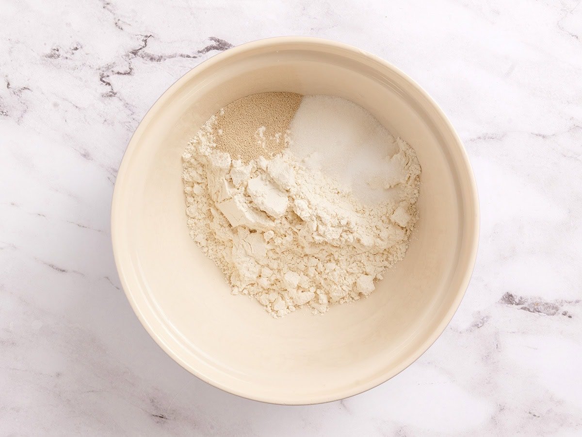 Mixing bowl filled with gluten free bread flour, sugar, salt, and instant yeast before combining.