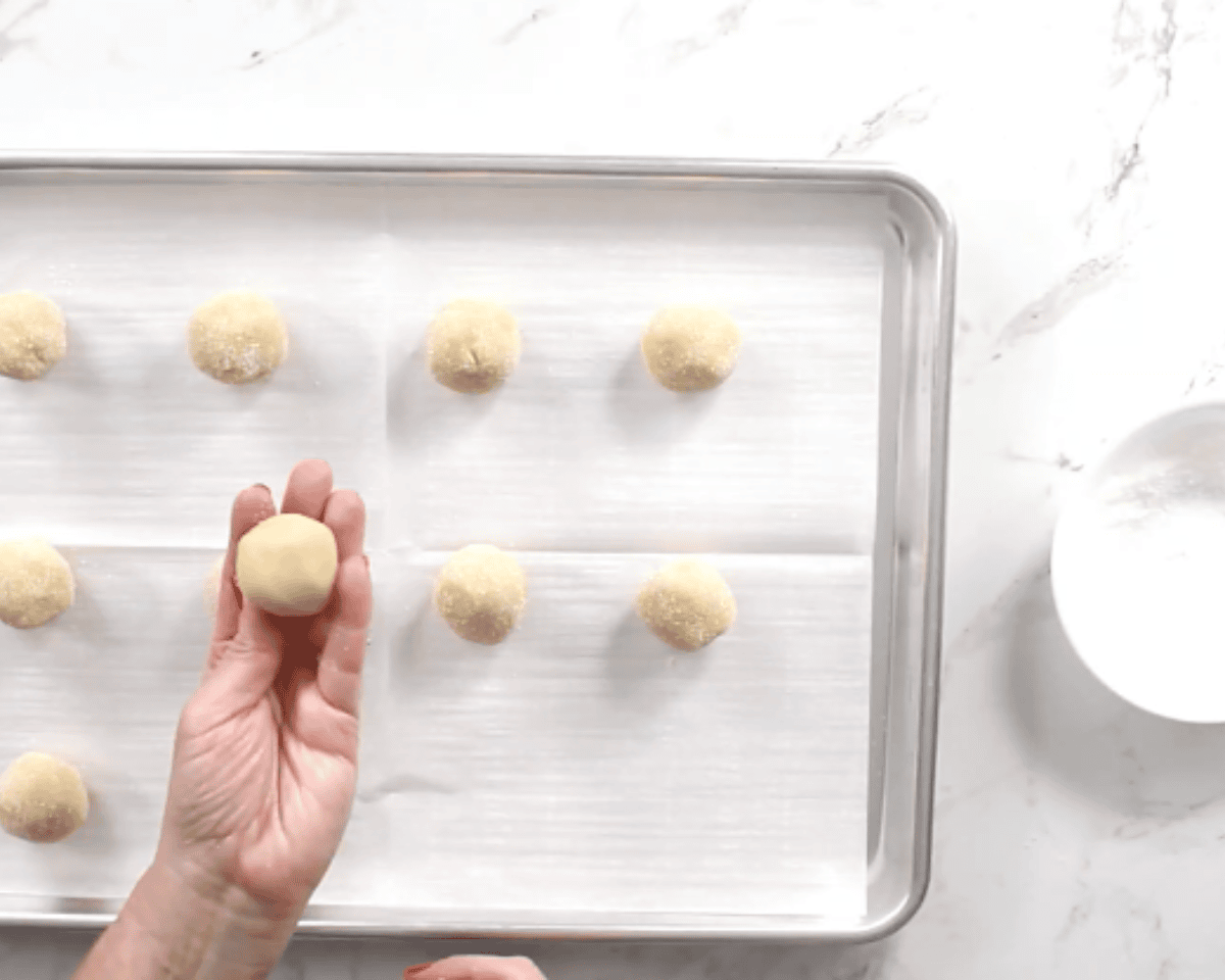 rolling gluten-free thumbprint cookies on a cookie sheet