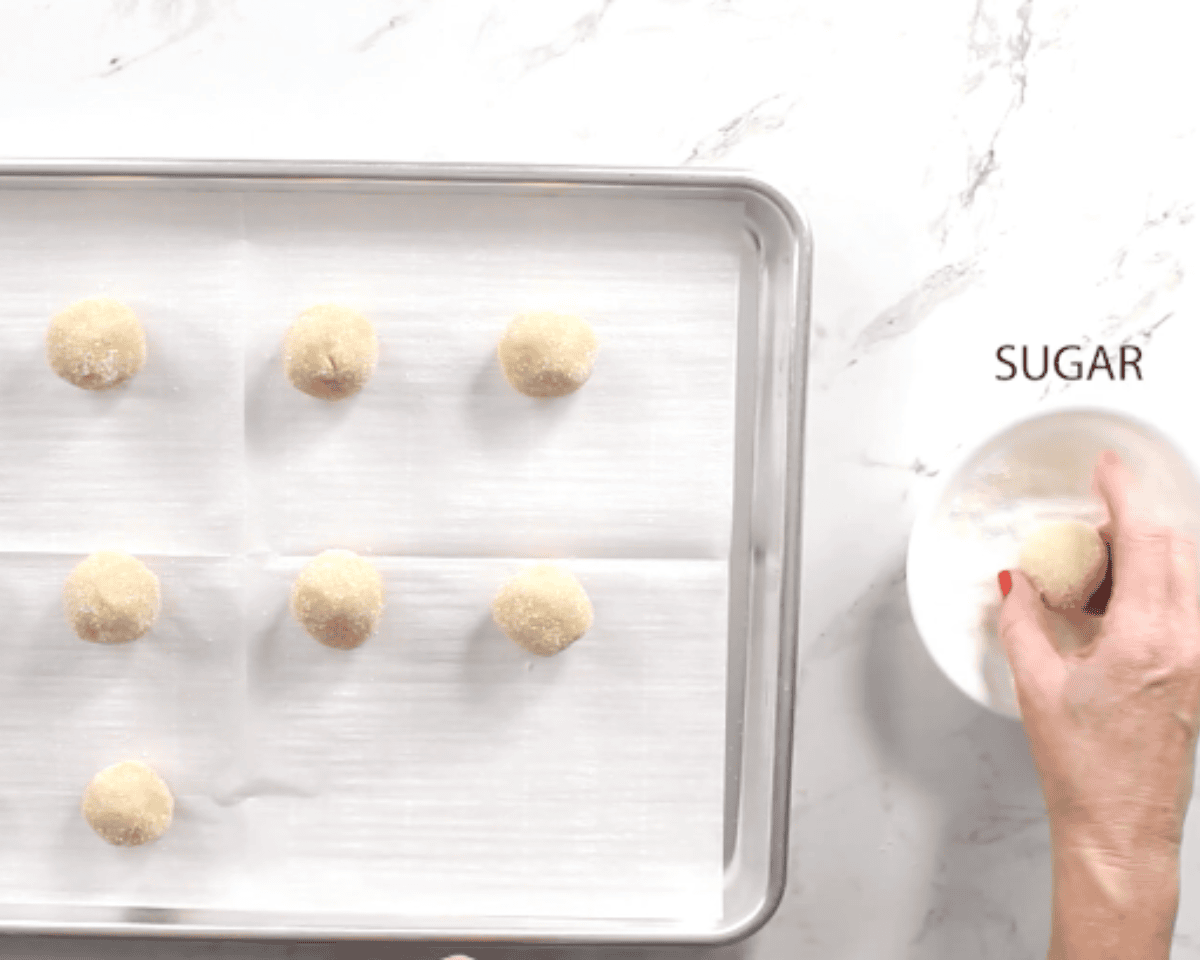 gluten-free thumbprint cookie dough balls being shaped on a cookie sheet