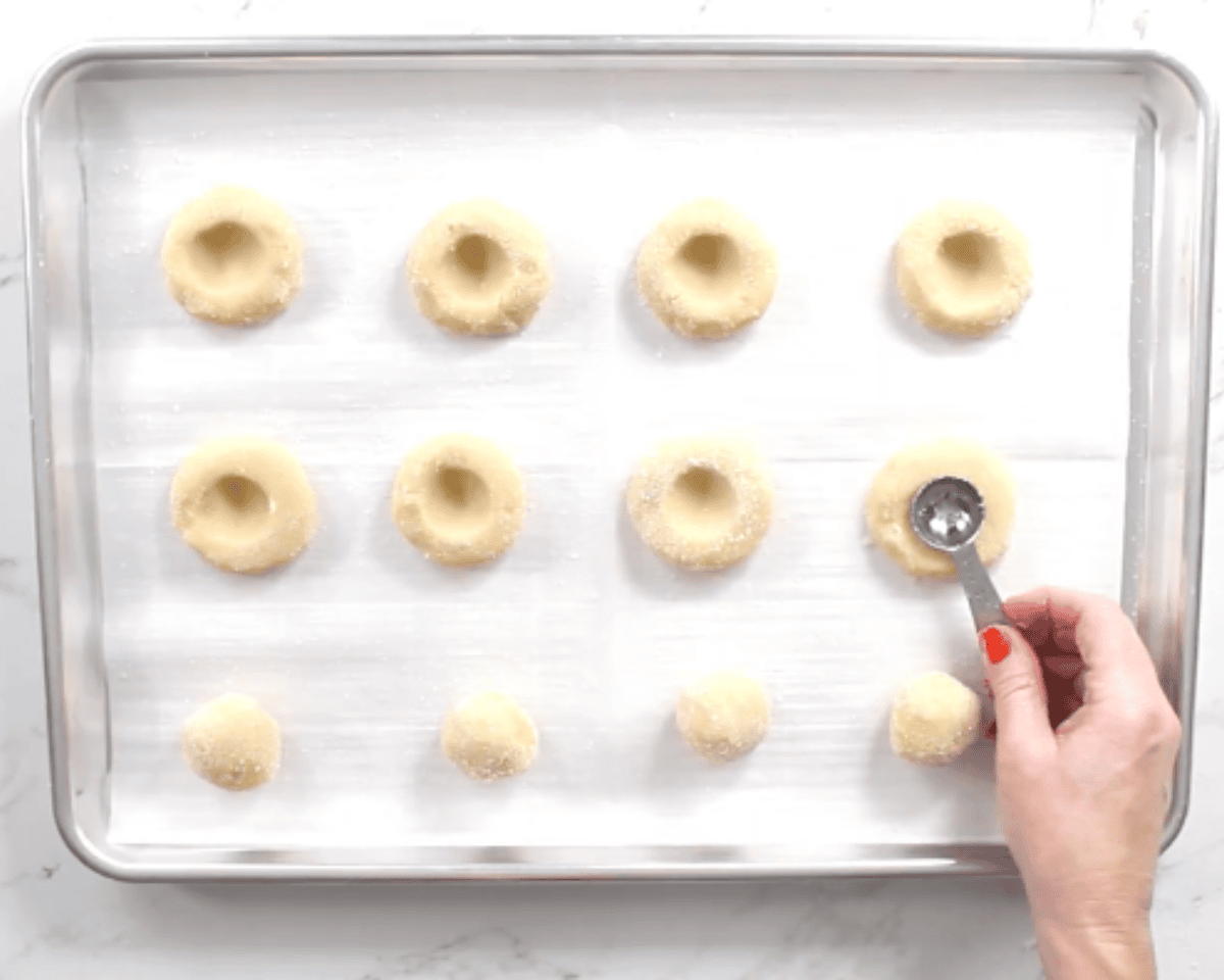 gluten-free thumbprint cookies on a cookie with a teaspoon being used to add a small indent for the jam