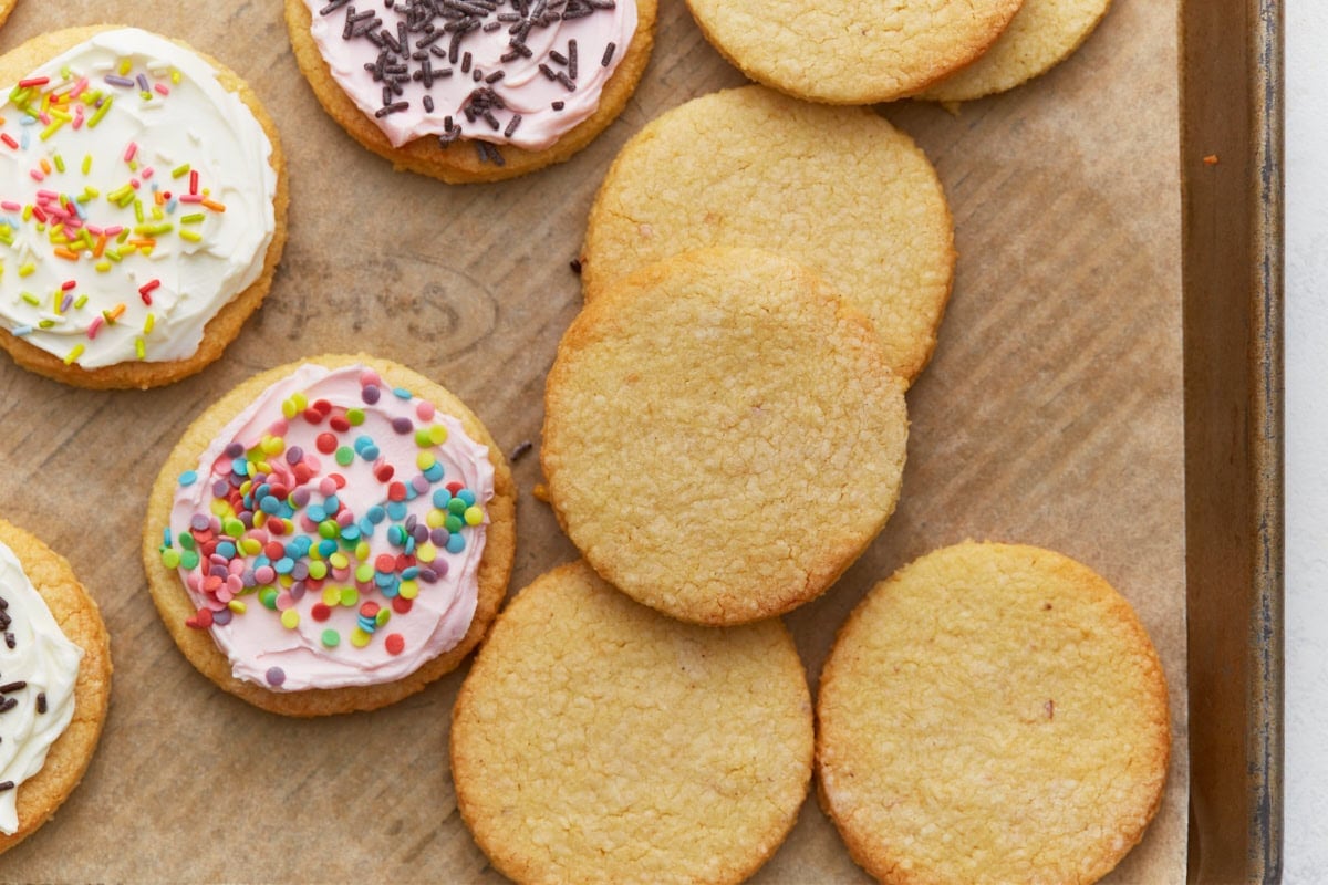 Frosted and unfrosted almond flour sugar cookies arranged on a parchment-lined baking sheet.
