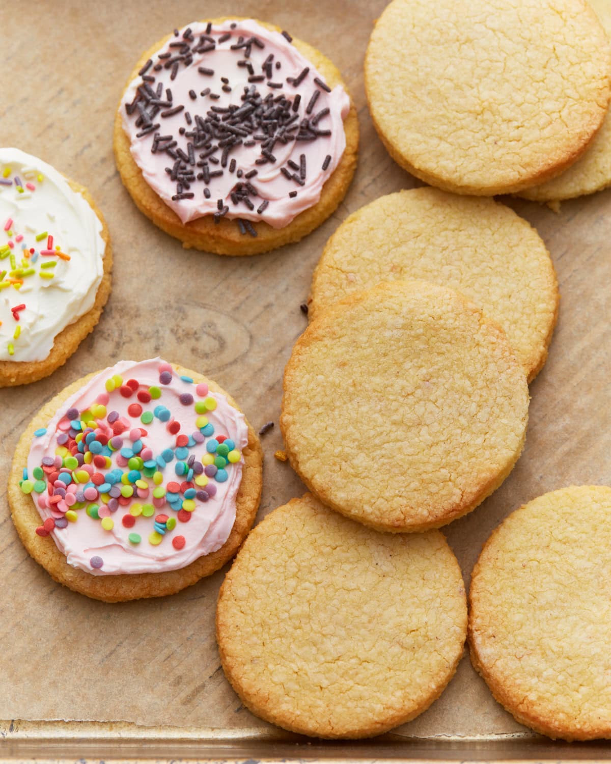 Frosted and unfrosted almond flour sugar cookies arranged on a parchment-lined baking sheet.