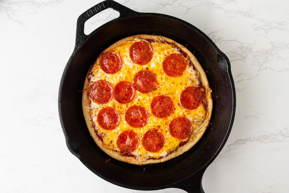 Baked chickpea pizza crust with melted cheese and pepperoni in a cast iron pan