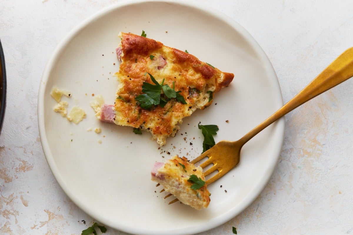 Slice of crustless ham and cheese quiche served on a plate with a fork.