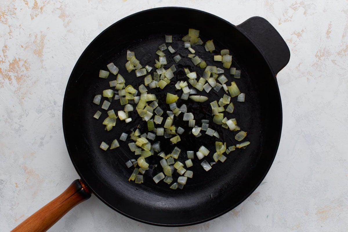 Diced onions sautéing in a skillet as the base for a crustless ham and cheese quiche.