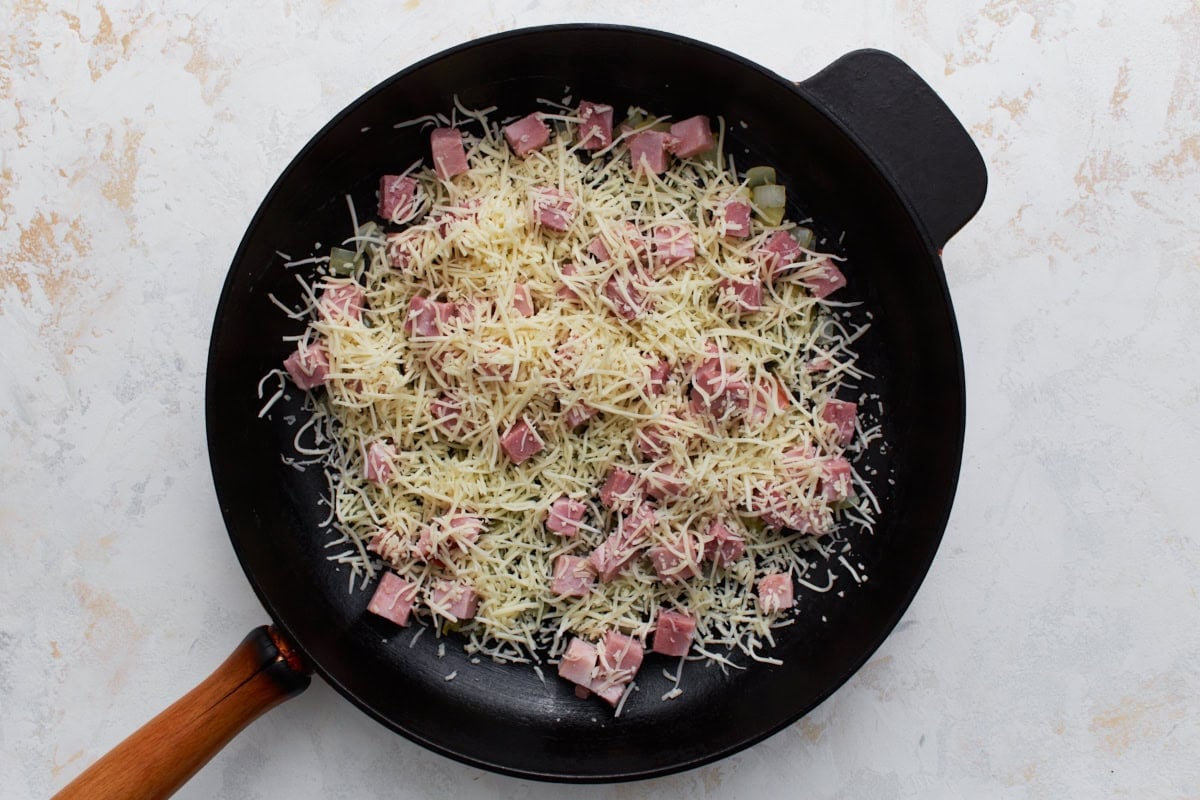 Diced ham and shredded cheese layered over sautéed onions in a skillet.