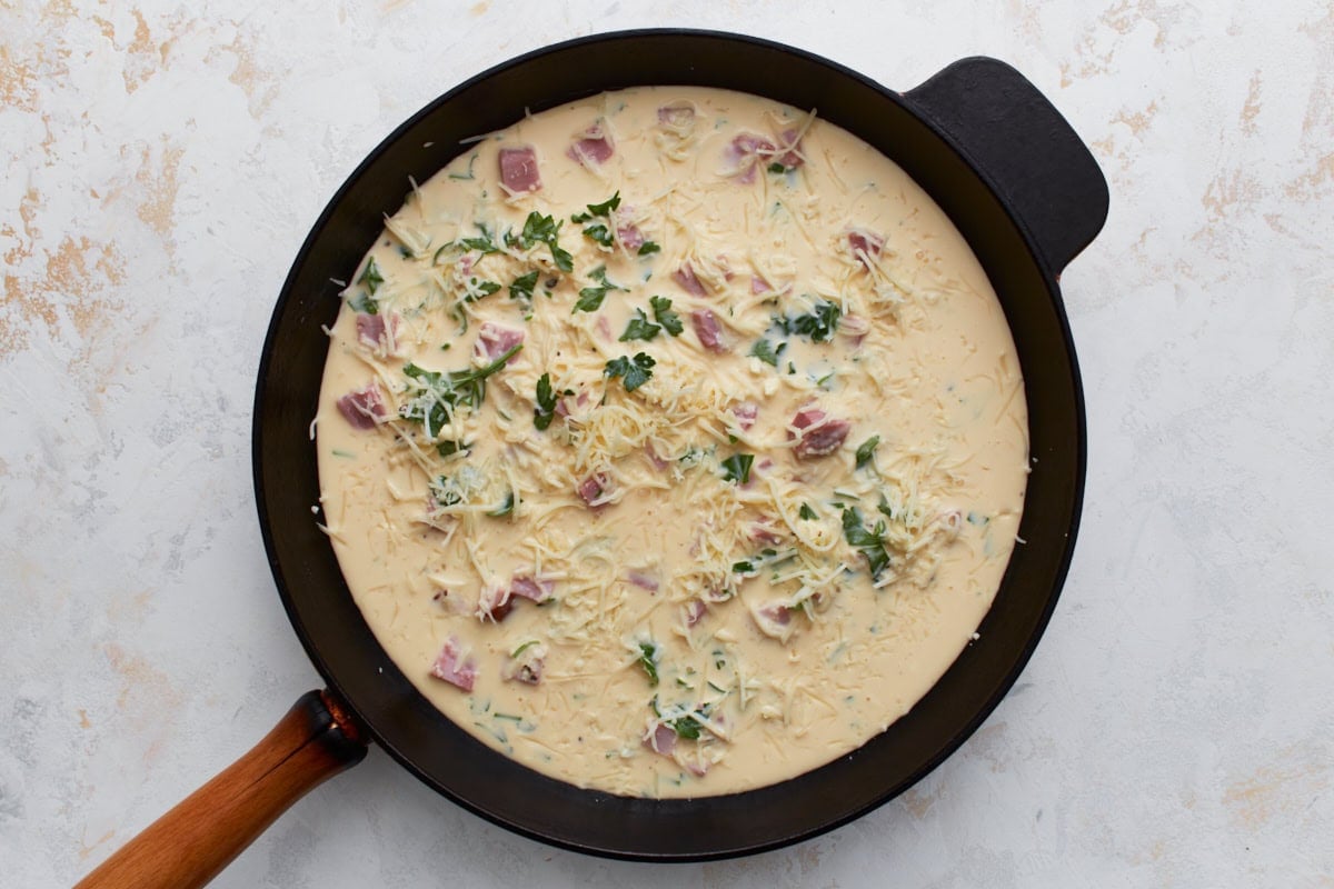 Unbaked crustless ham and cheese quiche with egg mixture poured into a skillet.