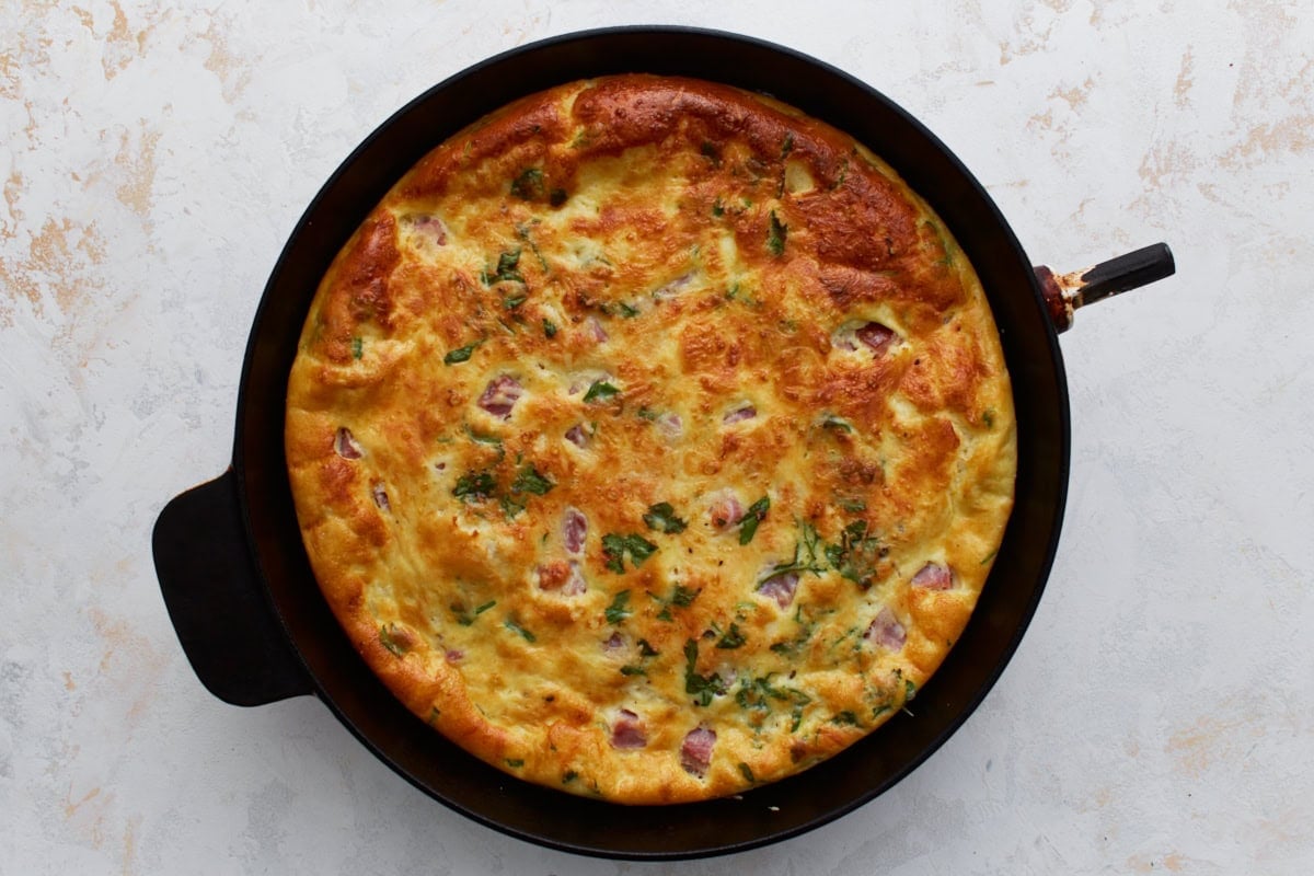 Golden brown crustless ham and cheese quiche baked in a skillet.