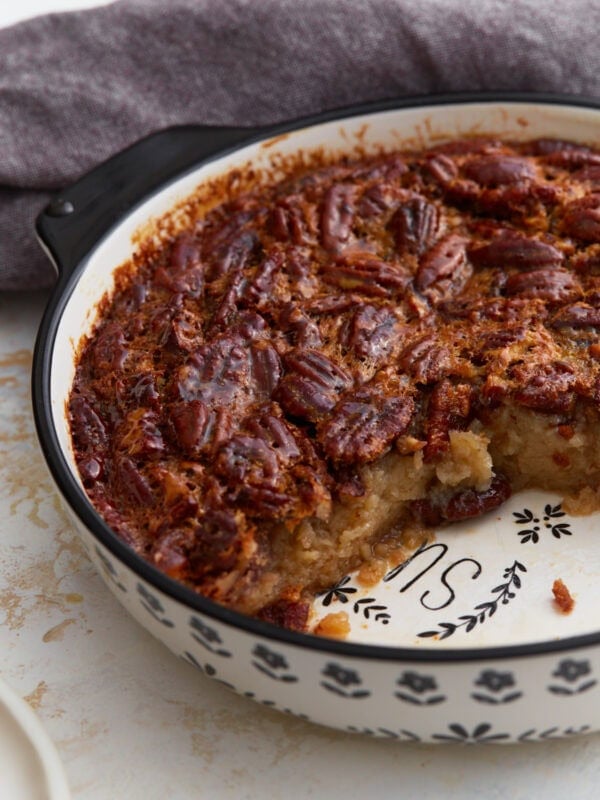 Crustless pecan pie baked in a ceramic pie dish with a slice removed, showing the gooey pecan filling