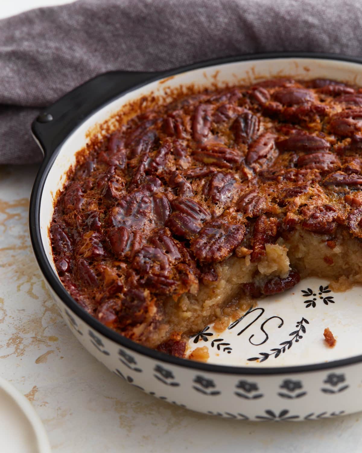 Crustless pecan pie baked in a ceramic pie dish with a slice removed, showing the gooey pecan filling