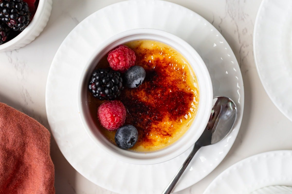 Dairy-free crème brûlée served in a white ramekin with a crackly sugar top and fresh berries on a plate.
