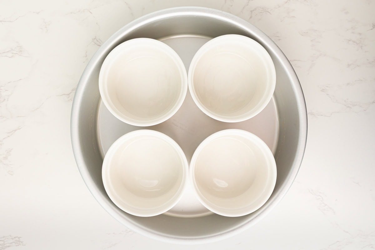 Four empty white ramekins arranged in a round baking dish