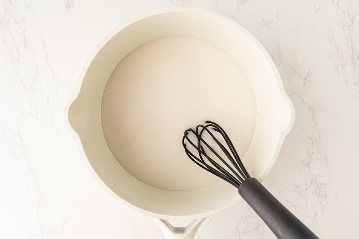 Full-fat coconut milk and sugar heating in a saucepan on the stovetop.