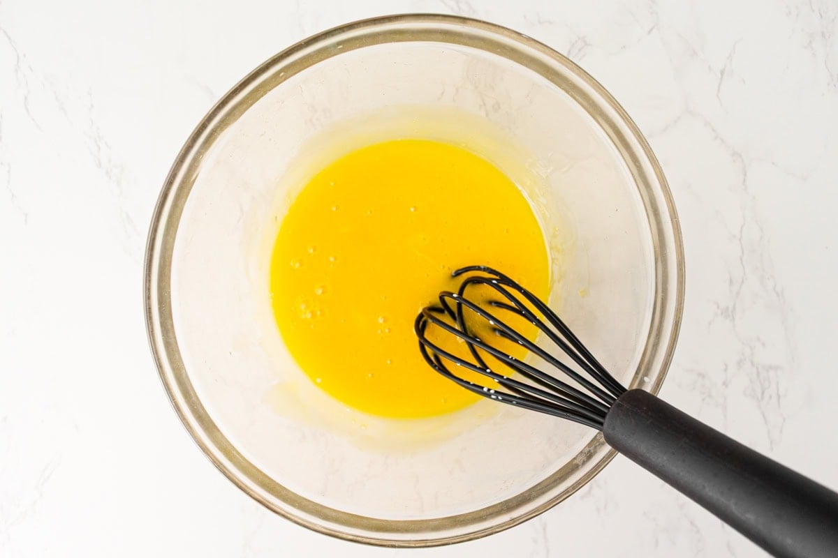 Egg yolks being whisked in a glass bowl for dairy-free crème brûlée.