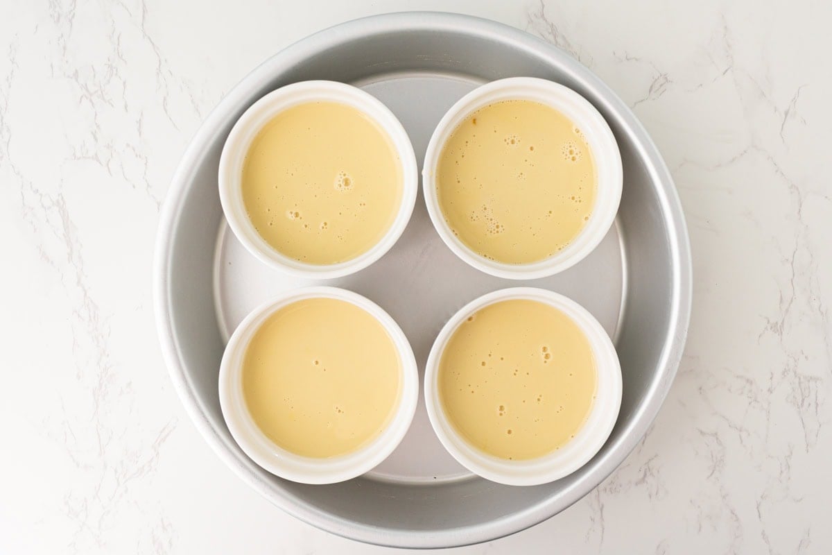 Dairy-free custard evenly poured into ramekins set inside a baking dish.