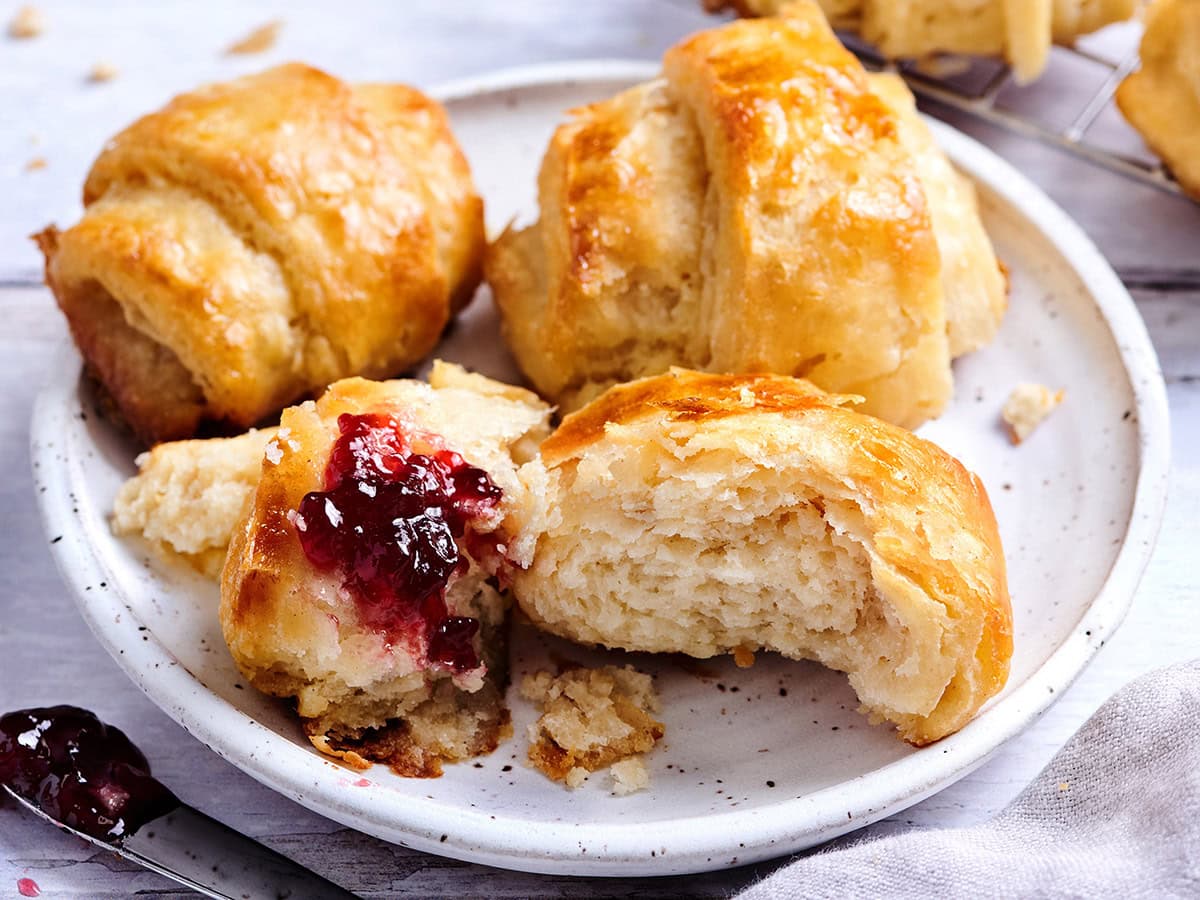 Warm gluten free croissants on a plate with one broken open and filled with berry jam to show the soft, flaky interior.