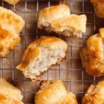 Gluten free croissants cooling on a wire rack with one croissant broken open to show the soft, flaky interior.