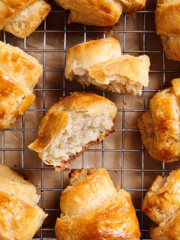 Gluten free croissants cooling on a wire rack with one croissant broken open to show the soft, flaky interior.