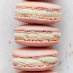 Close-up stack of pink French macarons with vanilla buttercream filling, showing smooth tops and crisp feet.