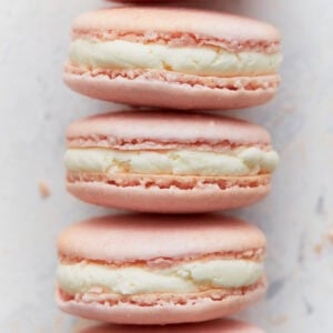 Close-up stack of pink French macarons with vanilla buttercream filling, showing smooth tops and crisp feet.