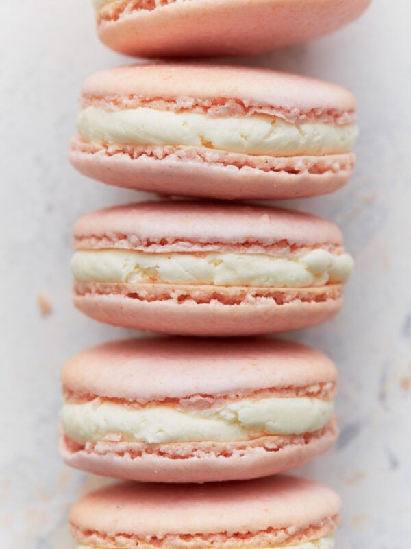 Close-up stack of pink French macarons with vanilla buttercream filling, showing smooth tops and crisp feet.