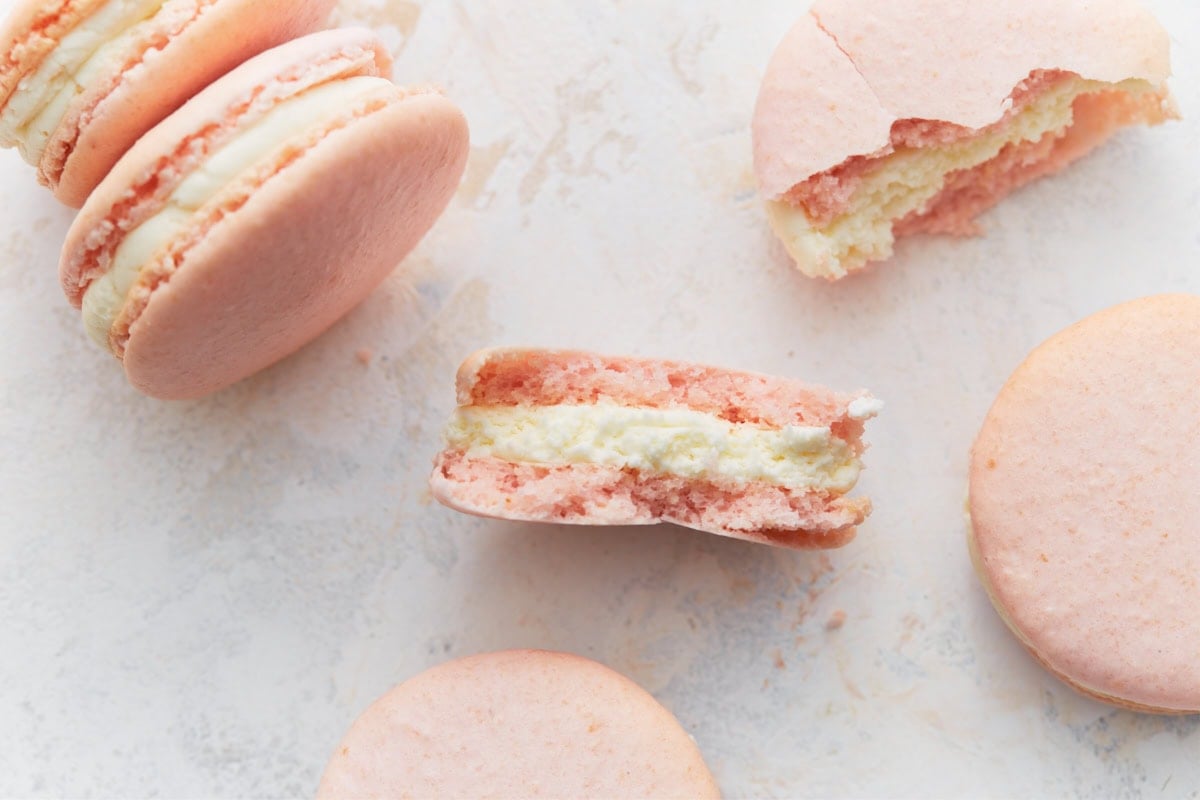 Close-up of macaron halves showing crisp shell and creamy buttercream center, with whole macarons around them.