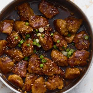 Gluten-free General Tso’s chicken coated in a glossy sweet and spicy sauce, garnished with green onions and sesame seeds in a skillet