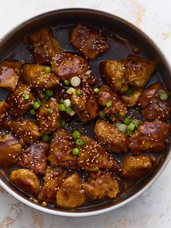 Gluten-free General Tso’s chicken coated in a glossy sweet and spicy sauce, garnished with green onions and sesame seeds in a skillet
