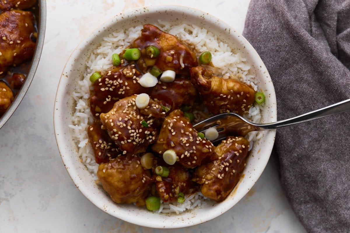 Gluten-free General Tso’s chicken served over white rice, topped with sesame seeds and sliced green onions
