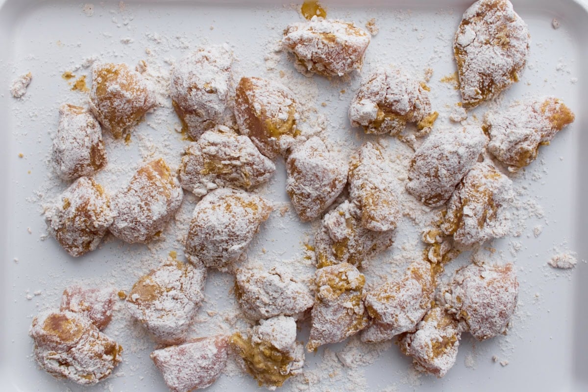 Raw chicken pieces coated in gluten-free flour and cornstarch mixture on a baking sheet