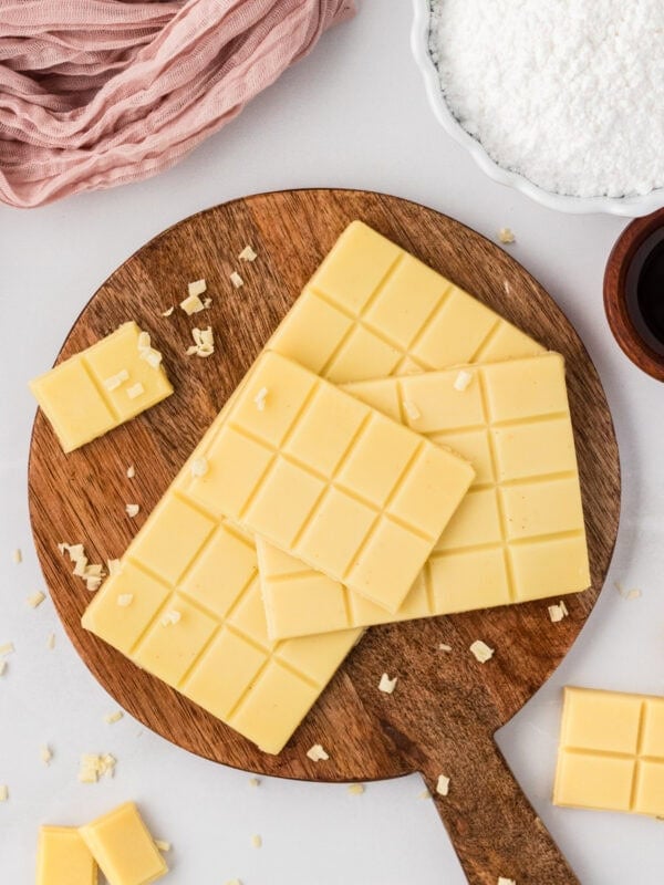 Vegan white chocolate bars stacked on a wooden board with small shaved pieces scattered around.