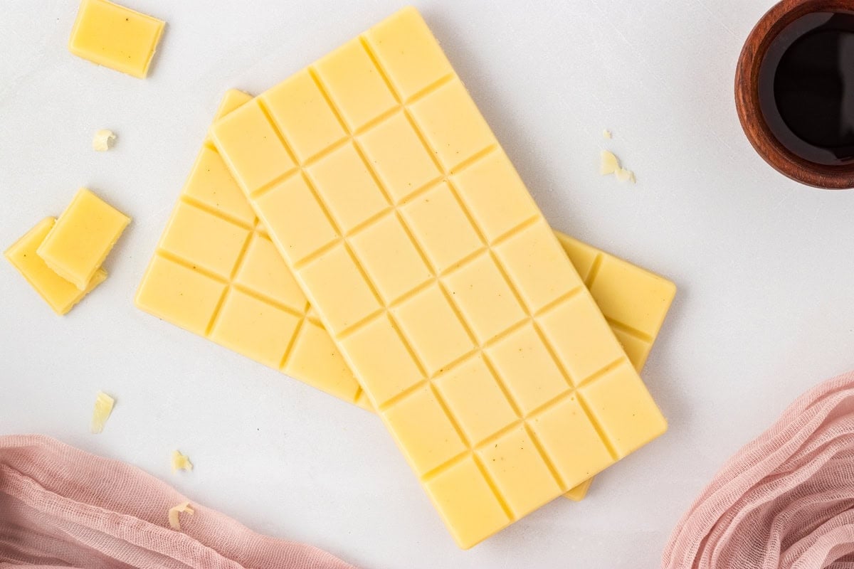 Two finished vegan white chocolate bars on a white surface with small broken pieces nearby.