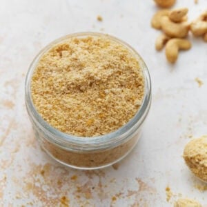 Jar filled with homemade vegan parmesan cheese made from cashews and nutritional yeast on a light countertop.