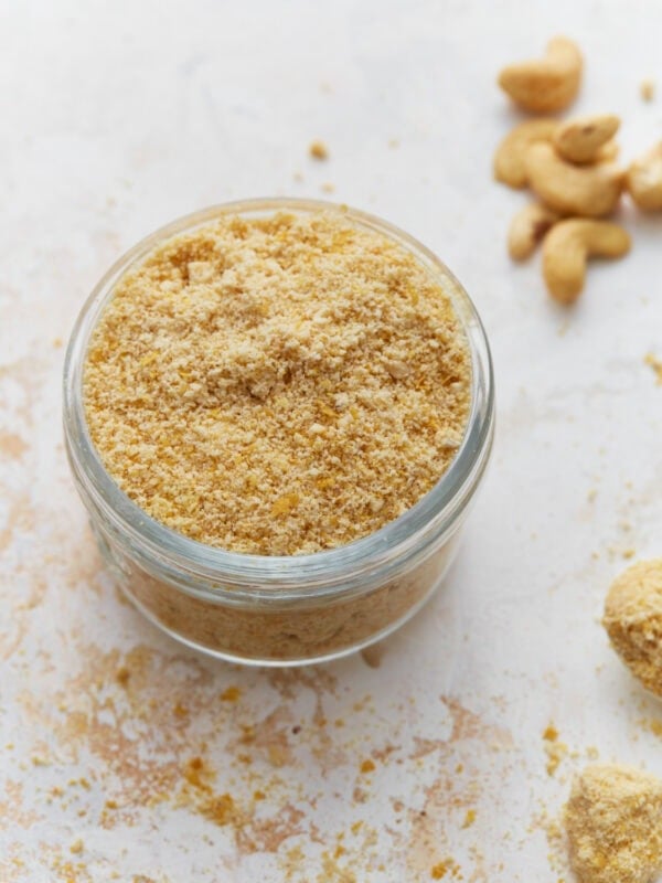 Jar filled with homemade vegan parmesan cheese made from cashews and nutritional yeast on a light countertop.