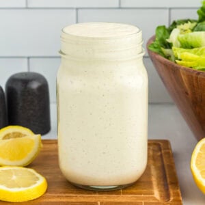 Mason jar of dairy-free Caesar dressing on a wooden board with lemon slices and romaine lettuce in the background