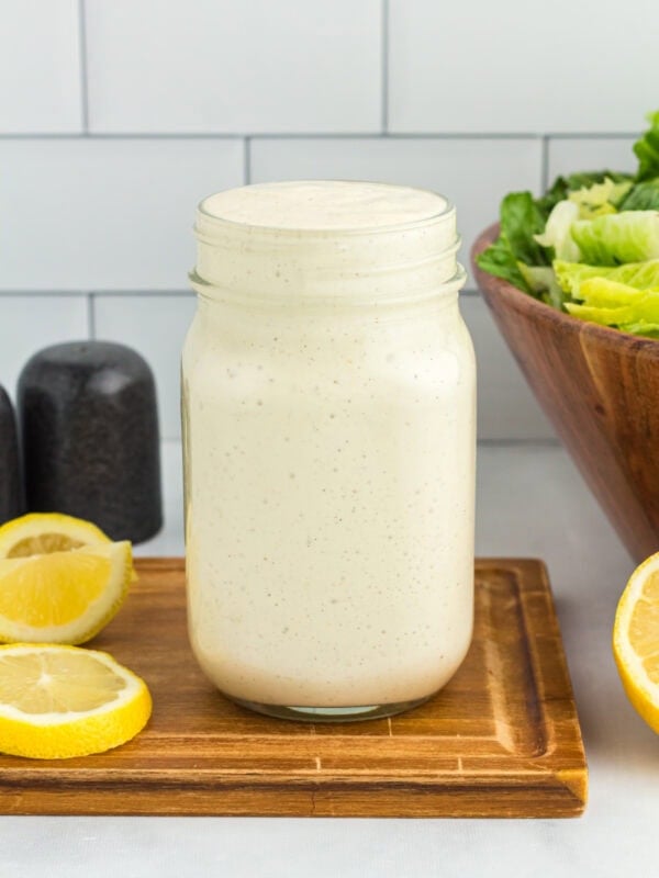Mason jar of dairy-free Caesar dressing on a wooden board with lemon slices and romaine lettuce in the background