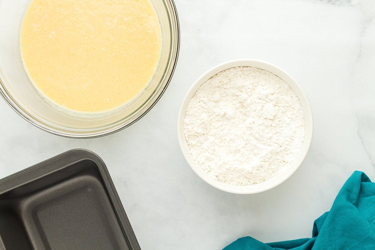 Gluten-free flour in a bowl next to a bowl of wet ingredients for cinnamon bread batter.