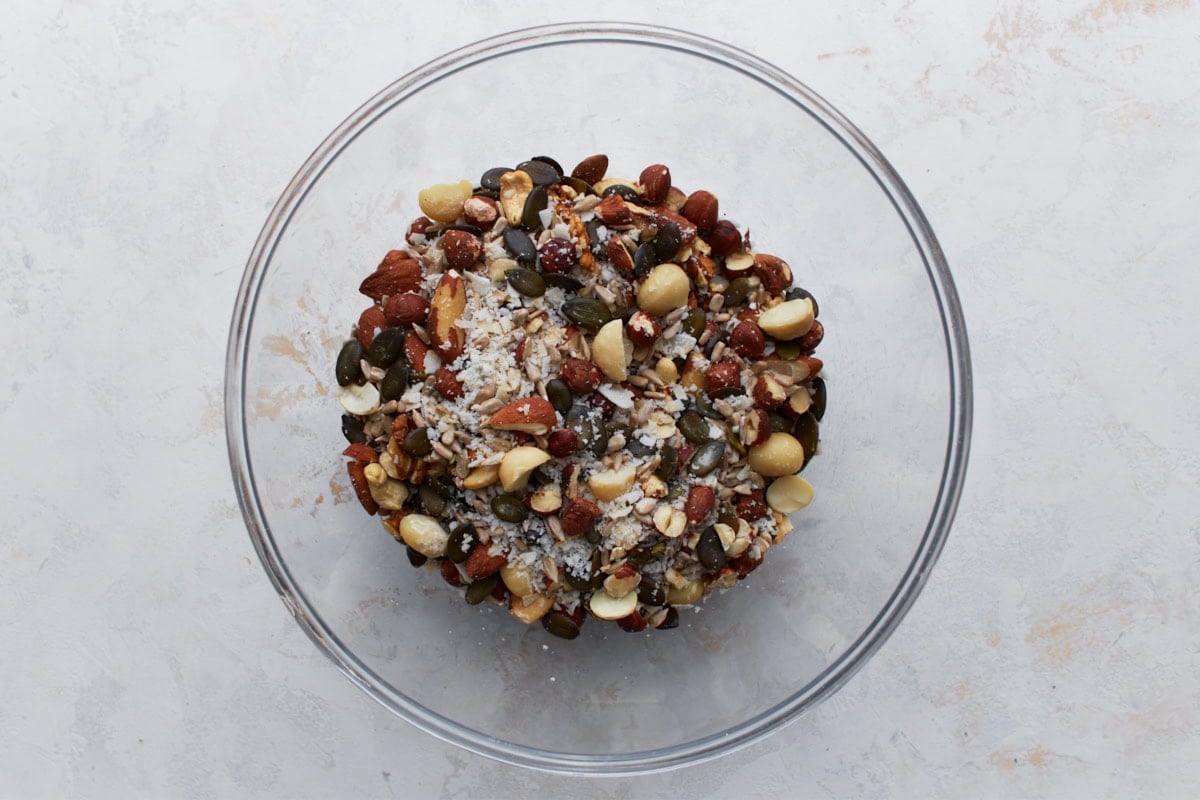 Unbaked keto granola ingredients in a glass bowl, including mixed nuts, seeds, and coconut flakes before mixing.