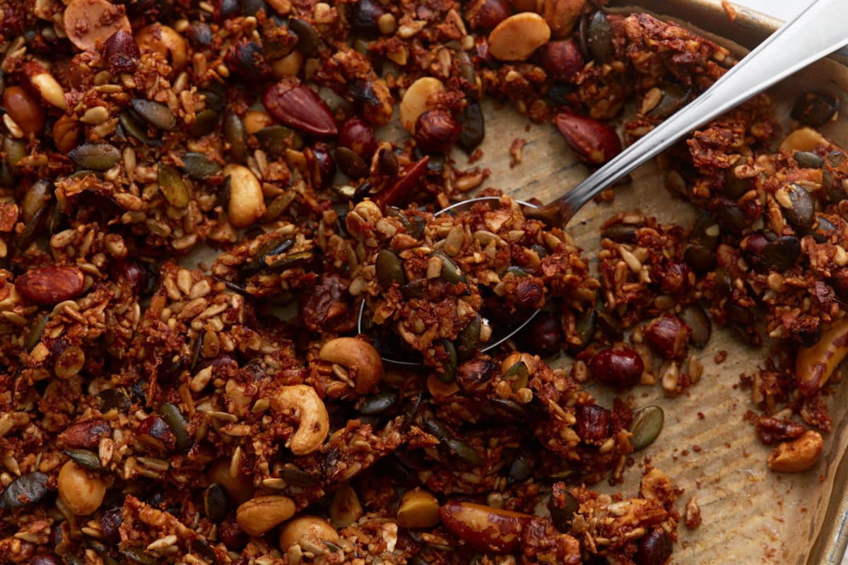 Spoon scooping chunky keto granola clusters from the baking sheet, highlighting texture and nut variety.