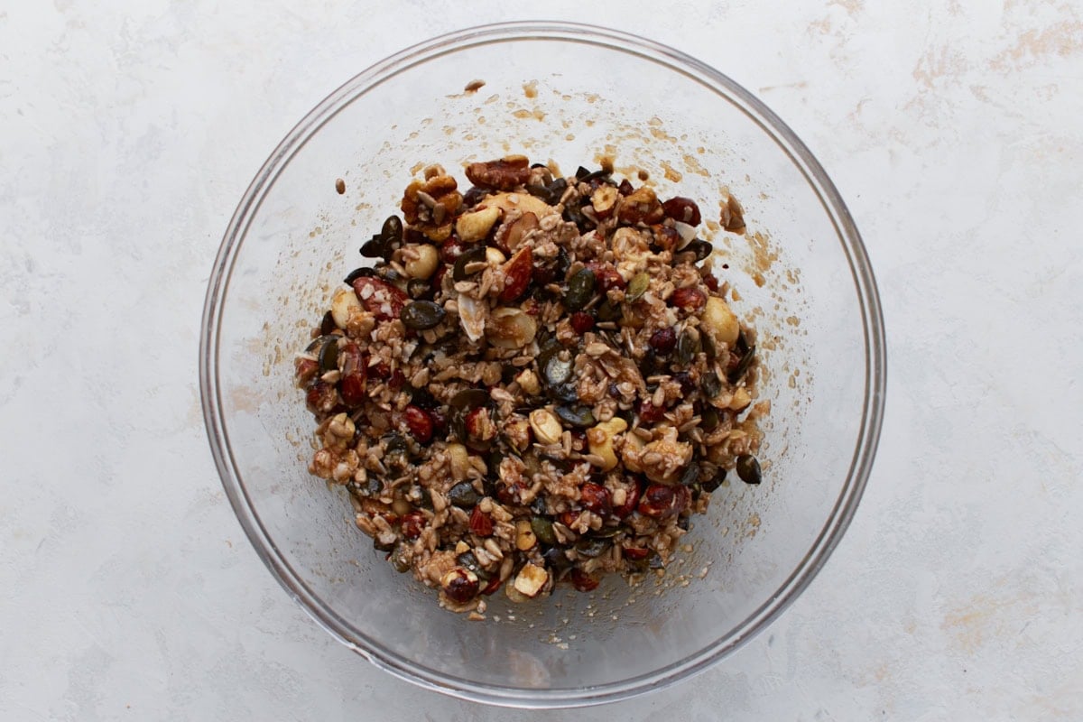 Keto granola mixture stirred together in a bowl, with nuts and seeds evenly coated in sweetener and oil.