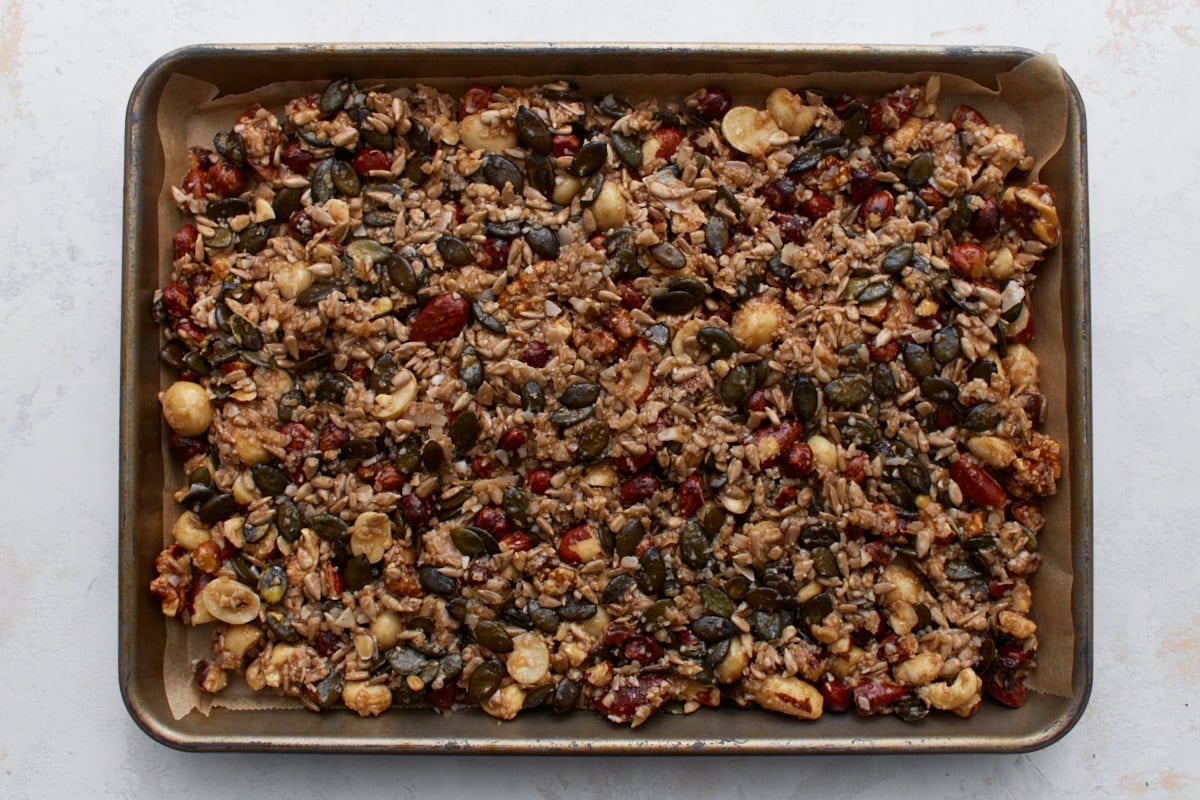 Keto granola spread evenly on a parchment-lined baking sheet before baking.